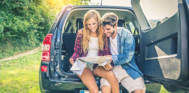 Young couple embracing on trunk of car while viewing a map.