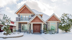 Suburban single-family home with wood and shingle siding, surrounded by snow under a partly cloudy sky.