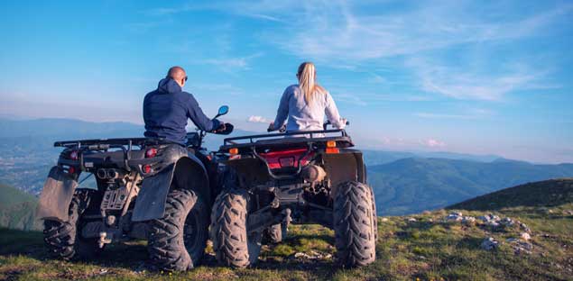 Couple riding 4-wheelers looking out into a mountainous distance.