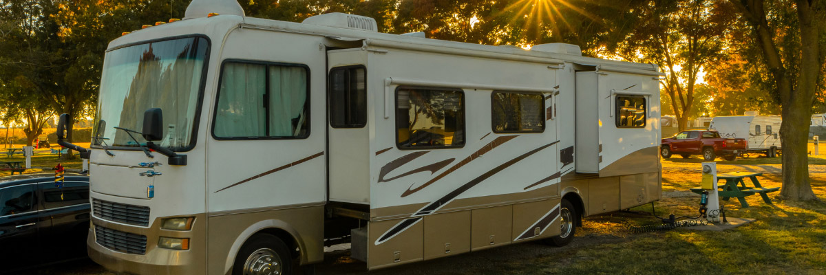 Recreational vehicle (RV) set up for camping, with the sun setting brightly through the autumn trees.